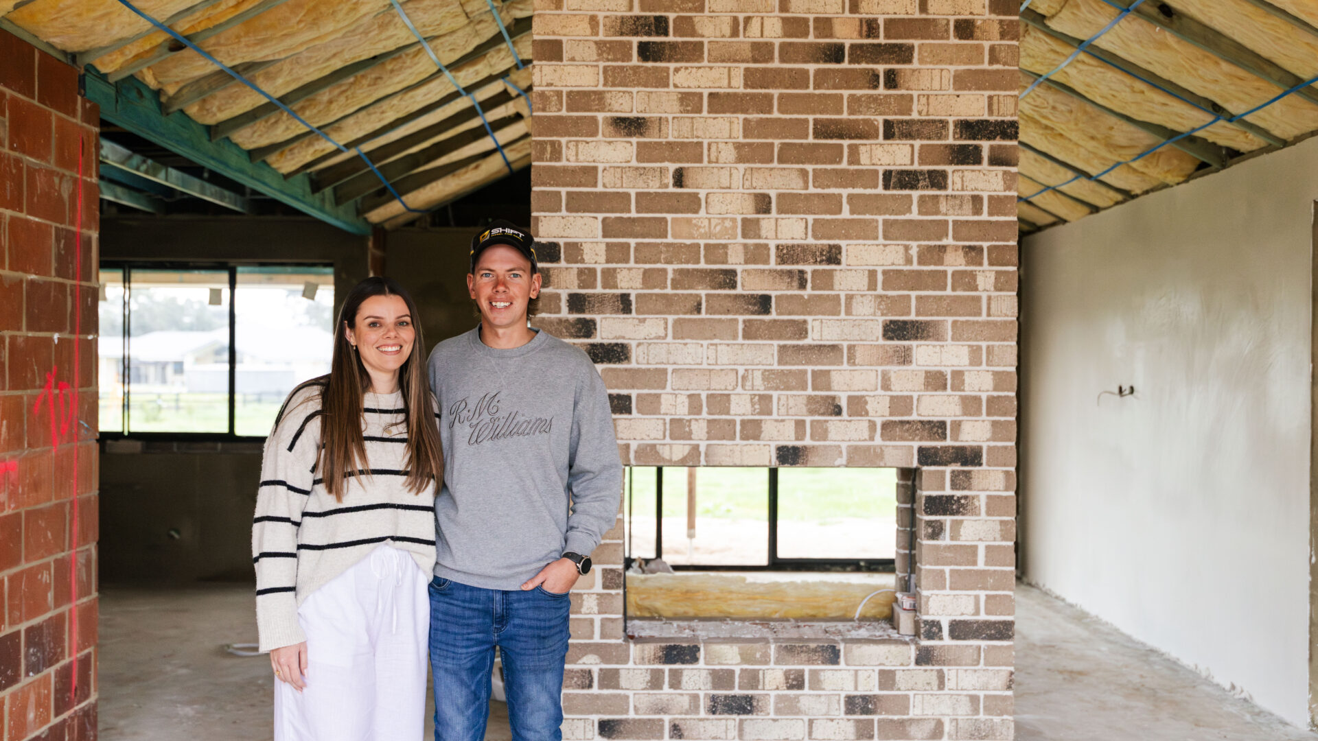 First-home buyers, Courtney and Hayden, beam proudly in front of their internal feature brick fireplace in their first home, built by WA Country Builders.
