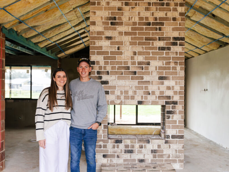 First-home buyers, Courtney and Hayden, beam proudly in front of their internal feature brick fireplace in their first home, built by WA Country Builders.