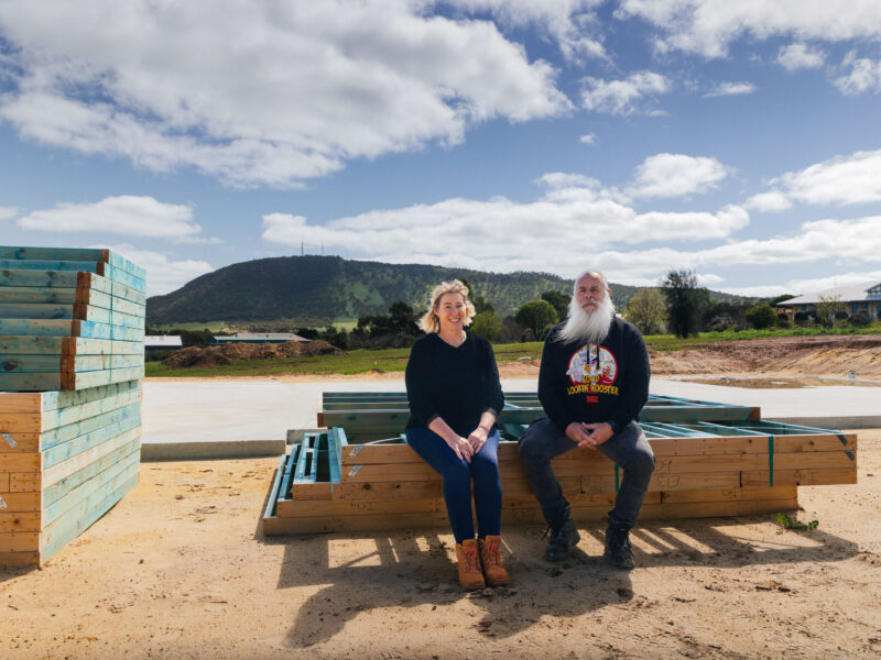 Kim & Rob, clients who built their new home in York, Western Australia, sit on the edge of some wood framing next to their freshly poured slab. The home is built by WA Country Builders.