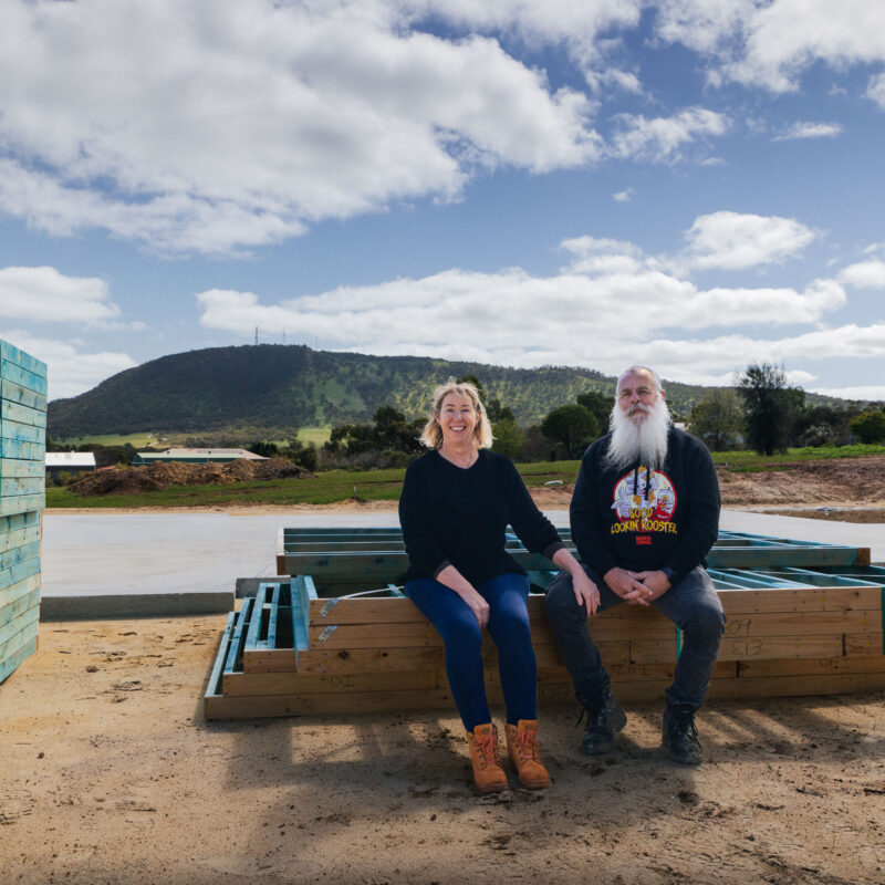 Kim & Rob, clients who built their new home in York, Western Australia, sit on the edge of some wood framing next to their freshly poured slab. The home is built by WA Country Builders.